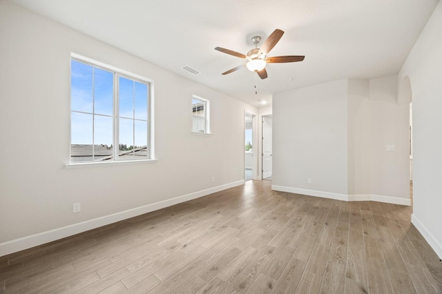 spare room featuring light wood-type flooring, visible vents, a ceiling fan, and baseboards