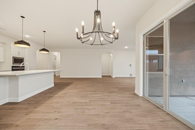 kitchen featuring white cabinets, a chandelier, arched walkways, light countertops, and stainless steel microwave
