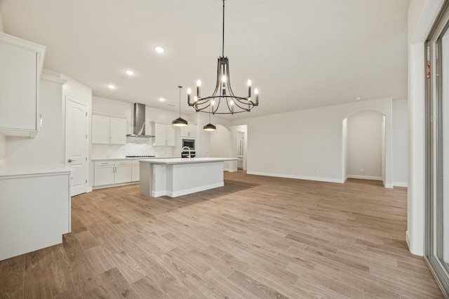 kitchen featuring a center island with sink, recessed lighting, white cabinetry, wall chimney range hood, and light countertops