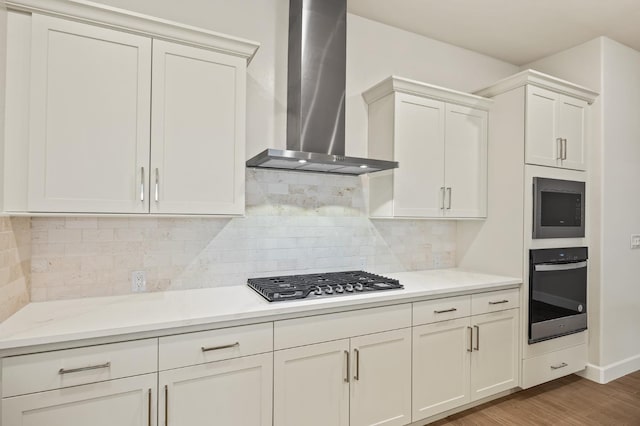 kitchen with wall chimney range hood, wood finished floors, stainless steel appliances, light countertops, and white cabinetry