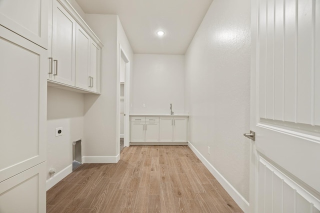 washroom featuring light wood-style flooring, a sink, baseboards, cabinet space, and electric dryer hookup