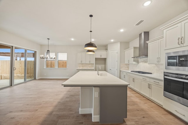 kitchen with wall chimney range hood, a sink, gas cooktop, a chandelier, and recessed lighting