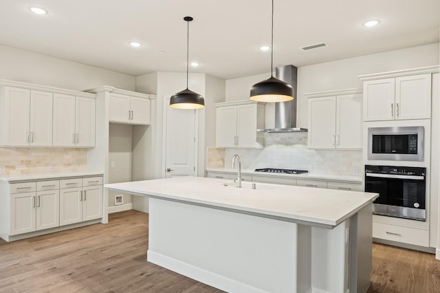 kitchen featuring oven, a sink, stainless steel microwave, wall chimney exhaust hood, and decorative backsplash