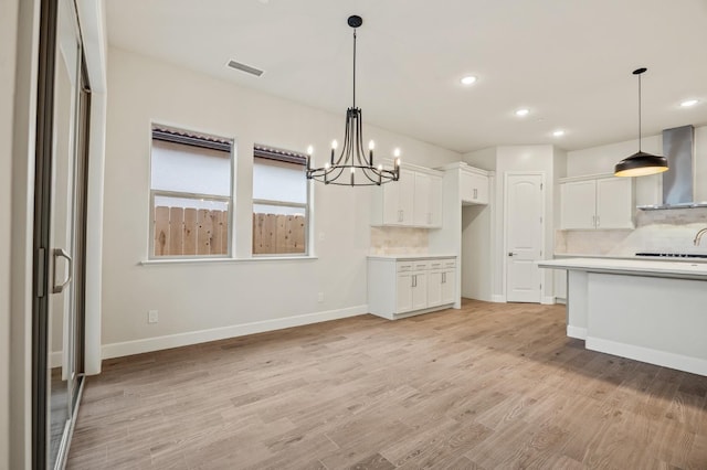 kitchen featuring wall chimney exhaust hood, tasteful backsplash, visible vents, a chandelier, and white cabinetry