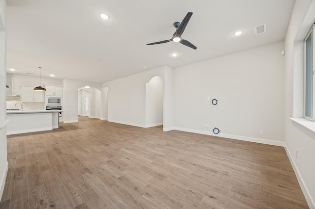 unfurnished living room with visible vents, arched walkways, recessed lighting, and ceiling fan
