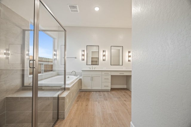 full bath featuring wood finished floors, a stall shower, a bath, a textured wall, and visible vents