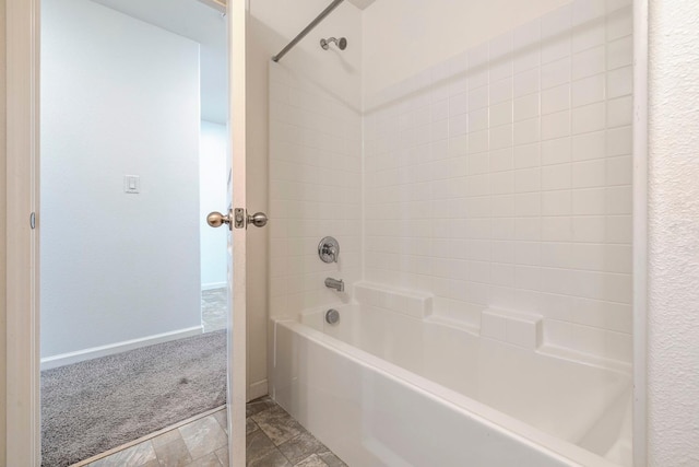 bathroom with washtub / shower combination, stone finish flooring, and baseboards