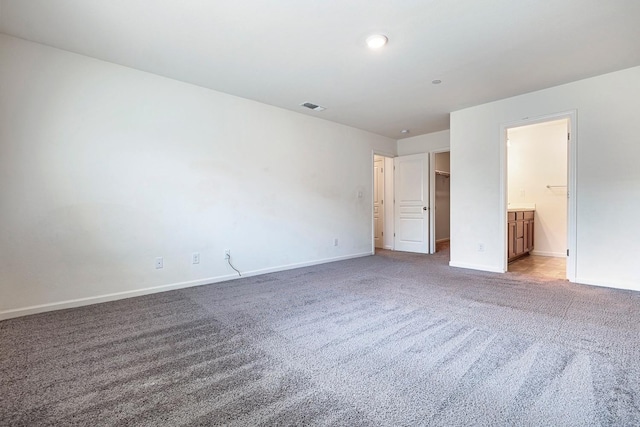unfurnished bedroom with carpet floors, baseboards, a walk in closet, and ensuite bath