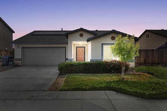 single story home with solar panels, concrete driveway, fence, an attached garage, and stucco siding