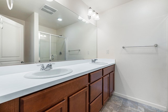 bathroom featuring baseboards, an enclosed shower, double vanity, and stone finish flooring