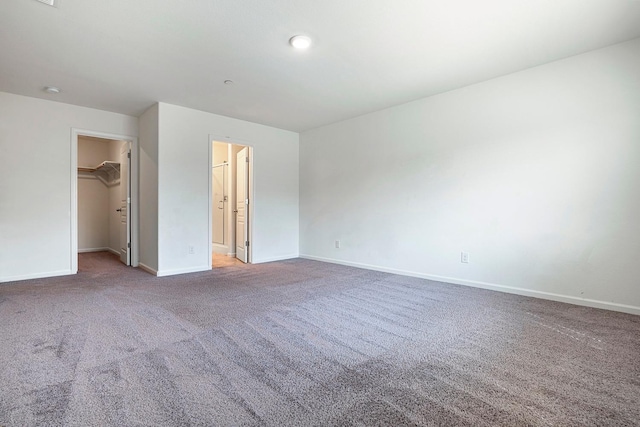 unfurnished bedroom featuring a walk in closet, carpet flooring, baseboards, and a closet
