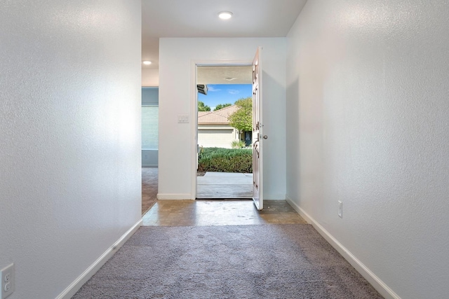 doorway with carpet, a textured wall, and baseboards