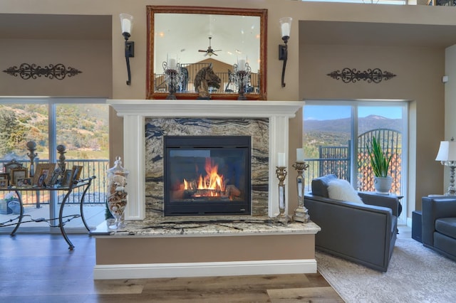 room details featuring ceiling fan, a high end fireplace, wood finished floors, baseboards, and a mountain view