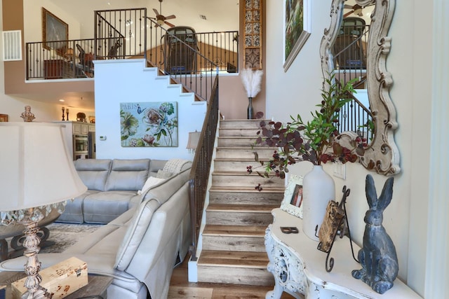 stairway featuring visible vents, a ceiling fan, a towering ceiling, and wood finished floors