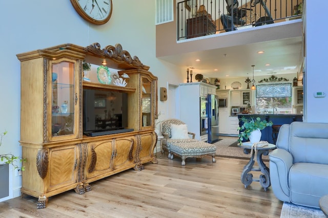 living area with light wood-type flooring, a high ceiling, and visible vents