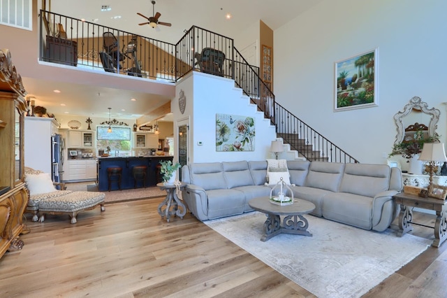 living room featuring visible vents, a high ceiling, stairway, light wood-type flooring, and a ceiling fan