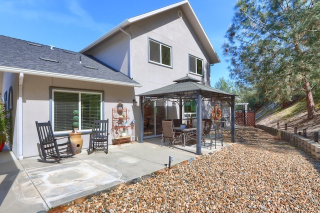 rear view of house with a gazebo, a shingled roof, a patio area, and stucco siding