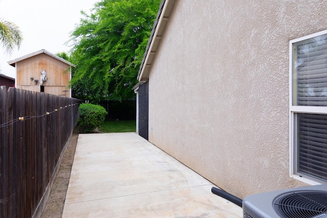 view of side of home featuring fence, a patio, central air condition unit, and stucco siding