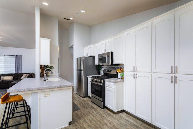 kitchen featuring wood finished floors, a sink, a breakfast bar, stainless steel appliances, and visible vents