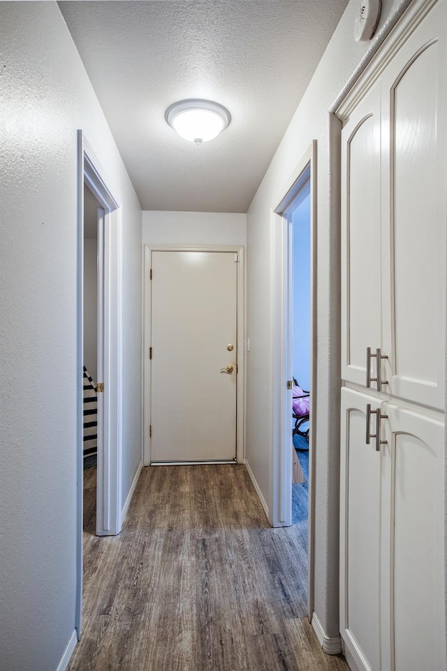 corridor featuring baseboards, a textured ceiling, and dark wood-style floors