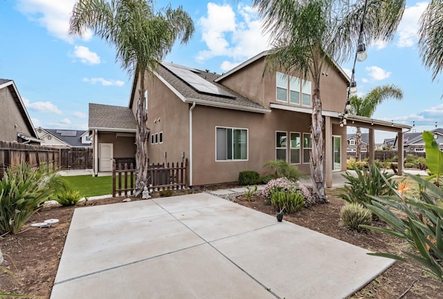 rear view of house with roof mounted solar panels, a patio, a fenced backyard, and stucco siding