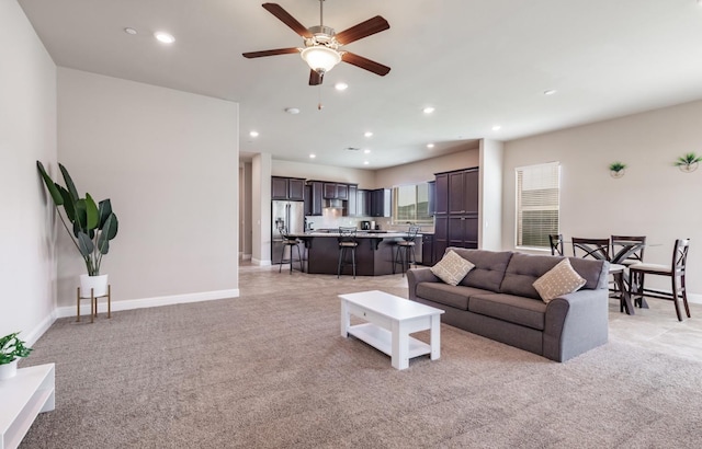living room with ceiling fan, baseboards, and light colored carpet
