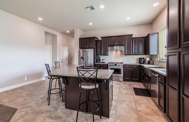 kitchen featuring high end appliances, dark brown cabinets, visible vents, wall chimney range hood, and a breakfast bar area