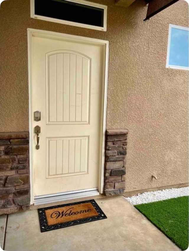 view of exterior entry with stone siding and stucco siding