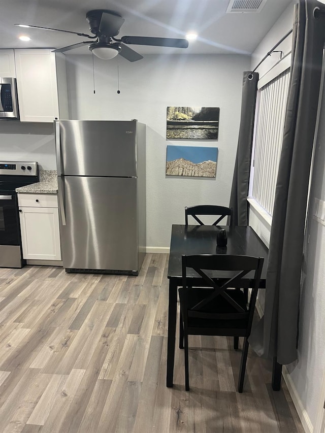 kitchen featuring baseboards, white cabinetry, a ceiling fan, light wood finished floors, and stainless steel appliances
