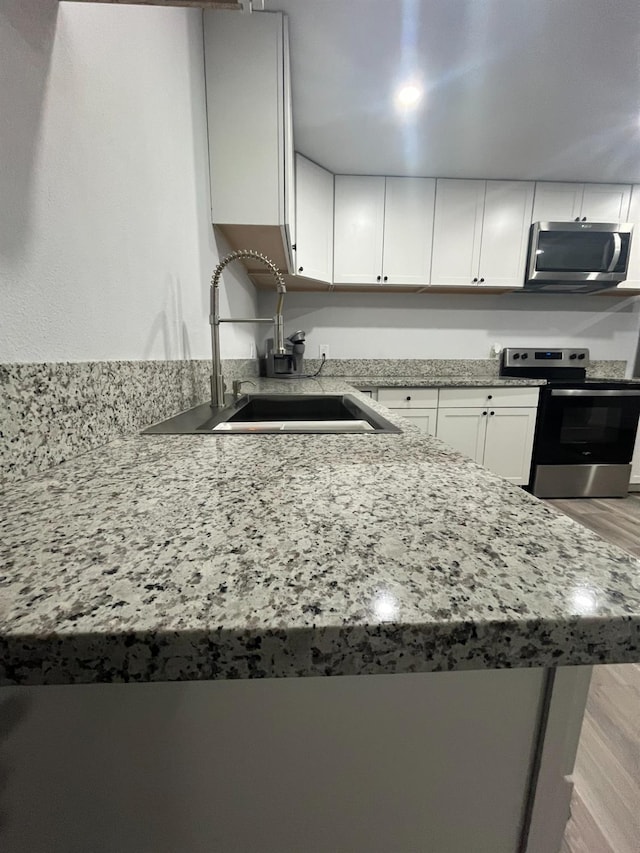kitchen featuring appliances with stainless steel finishes, light stone countertops, light wood-type flooring, a sink, and white cabinetry