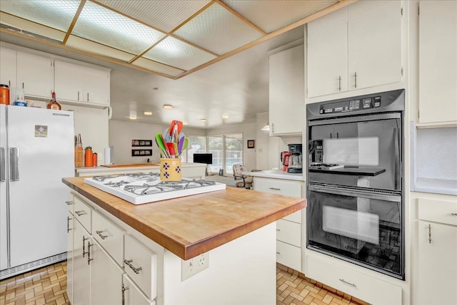 kitchen featuring white cabinets, butcher block countertops, white appliances, a kitchen island, and brick patterned floor