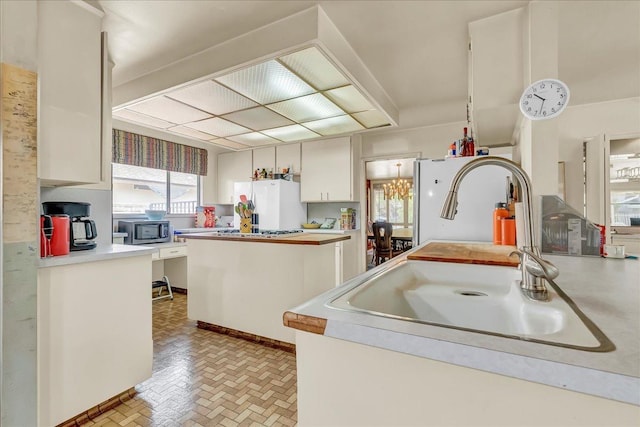 kitchen with brick patterned floor, light countertops, a sink, stainless steel microwave, and freestanding refrigerator
