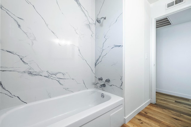 bathroom with baseboards, wood finished floors, visible vents, and shower / bathtub combination