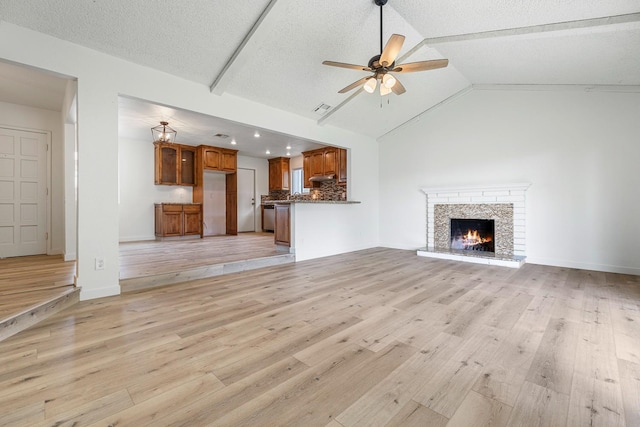 unfurnished living room with a warm lit fireplace, vaulted ceiling, a ceiling fan, and light wood-type flooring