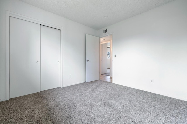 unfurnished bedroom featuring a textured ceiling, visible vents, carpet floors, and a closet