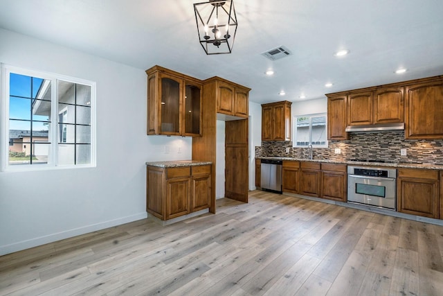 kitchen with a sink, brown cabinets, stainless steel appliances, under cabinet range hood, and visible vents