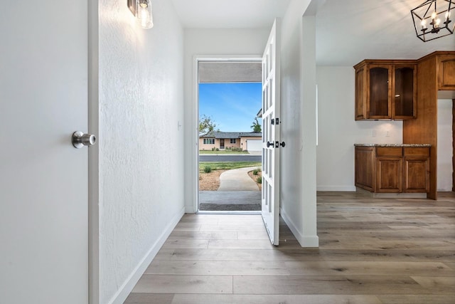 doorway featuring light wood finished floors, a textured wall, baseboards, and a chandelier