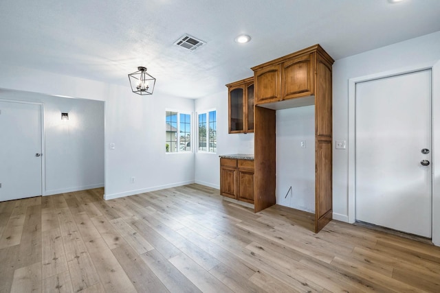 kitchen with visible vents, light wood-style floors, glass insert cabinets, a chandelier, and brown cabinetry