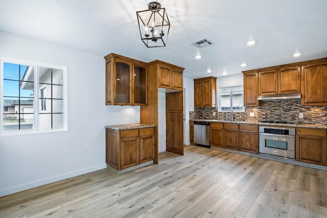 kitchen with tasteful backsplash, brown cabinets, stainless steel appliances, under cabinet range hood, and visible vents