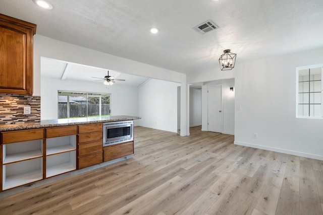 kitchen with brown cabinets, visible vents, stainless steel microwave, light wood-style floors, and decorative backsplash