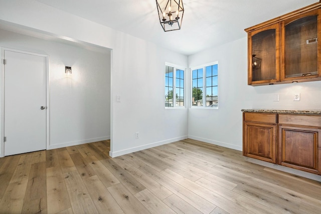 unfurnished dining area featuring an inviting chandelier, light wood-style floors, visible vents, and baseboards