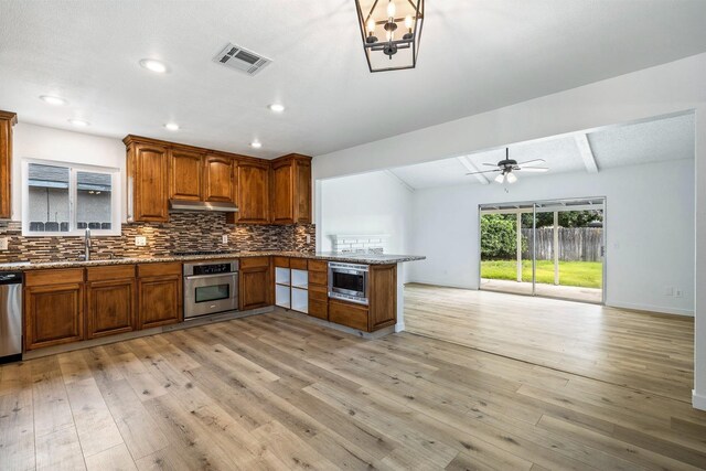 kitchen with open floor plan, visible vents, backsplash, brown cabinetry, and appliances with stainless steel finishes