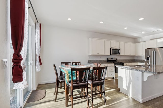 kitchen with white cabinets, light wood finished floors, appliances with stainless steel finishes, and dark stone countertops