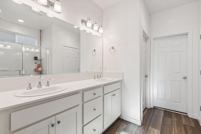 bathroom featuring wood finished floors, a sink, a shower stall, and double vanity