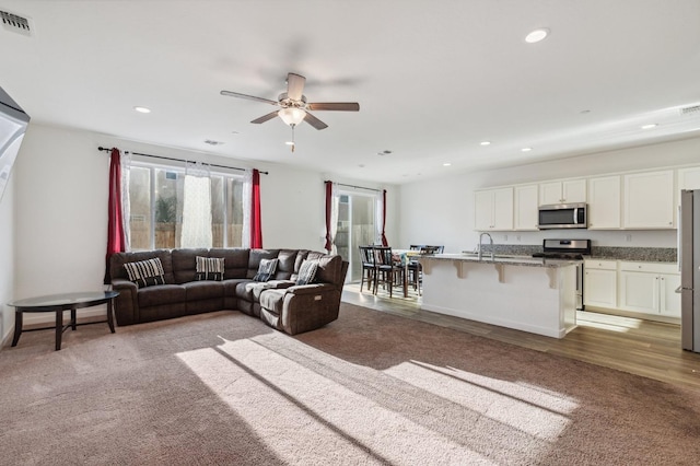 carpeted living room featuring a ceiling fan, visible vents, and recessed lighting