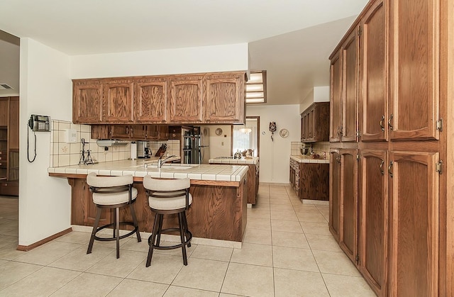 7355 N Pacific Ave, Fresno, CA 93711 - kitchen featuring tasteful backsplash, tile countertops, light tile patterned floors, a breakfast bar area, and a peninsula