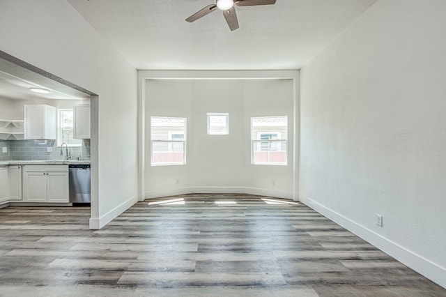 unfurnished dining area with light wood-style flooring, baseboards, ceiling fan, and a sink