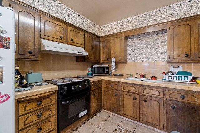 4311 N Emerson Ave, Fresno, CA 93705 - kitchen featuring under cabinet range hood, tile countertops, stainless steel microwave, black electric range, and tasteful backsplash