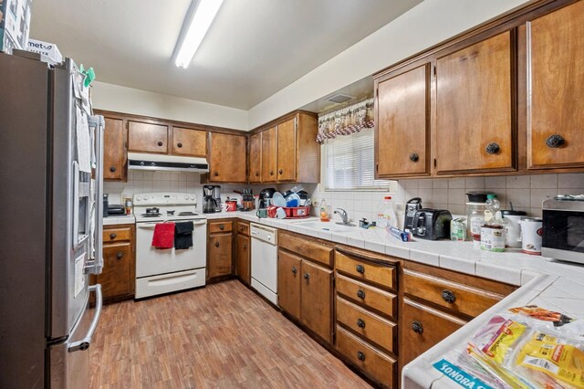 4311 N Emerson Ave, Fresno, CA 93705 - kitchen featuring a sink, brown cabinetry, appliances with stainless steel finishes, backsplash, and under cabinet range hood