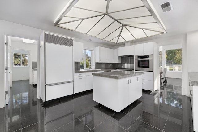 kitchen featuring oven, visible vents, built in refrigerator, a kitchen island, and white cabinetry